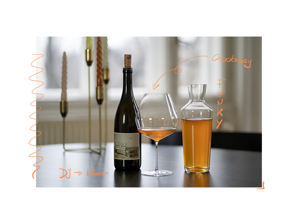 Eine Flasche "Entering the Nudist Area" Chardonnay von Mike Muff, daneben ein großes, mit dem Orange Wine gefülltes Glas von Mark Thomas und eine volle Zalto-Karaffe.